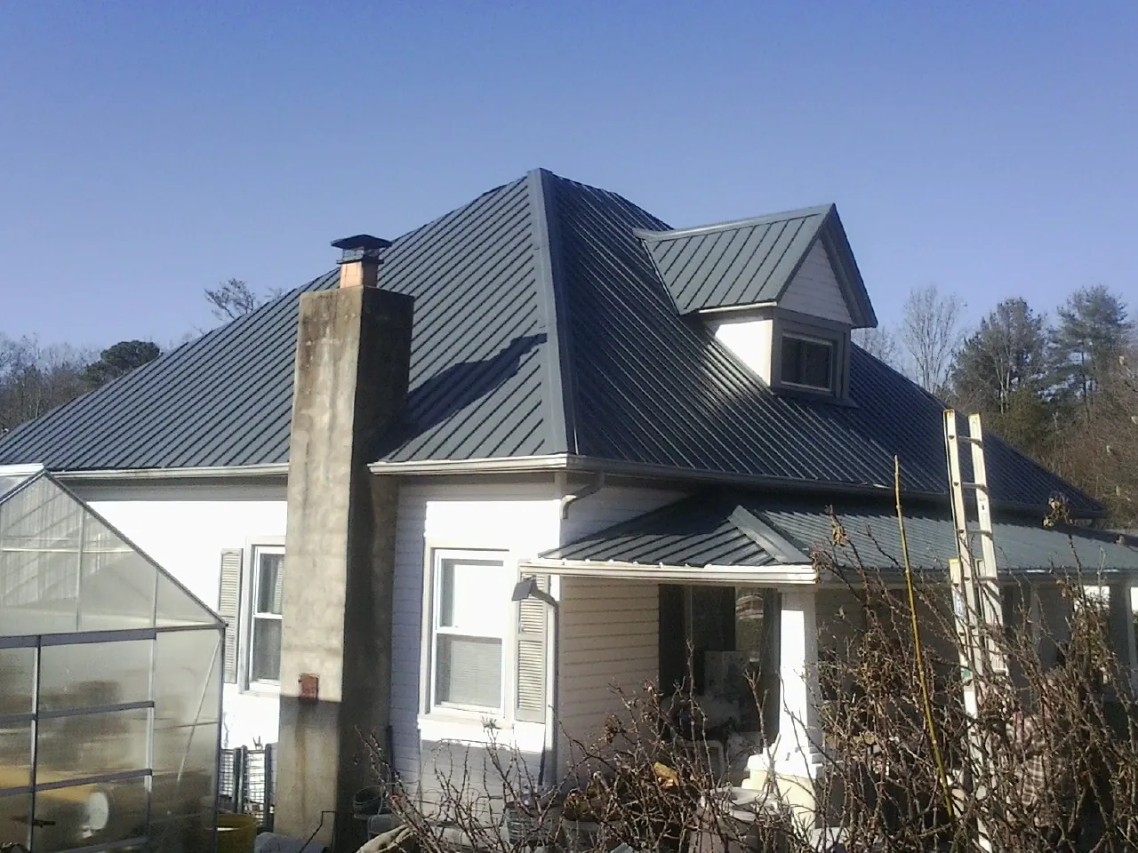 Dark blue standing seam metal roof on a white farmhouse with dormer — Slate & Tile Roof Repair by Roofing Brothers in Mears