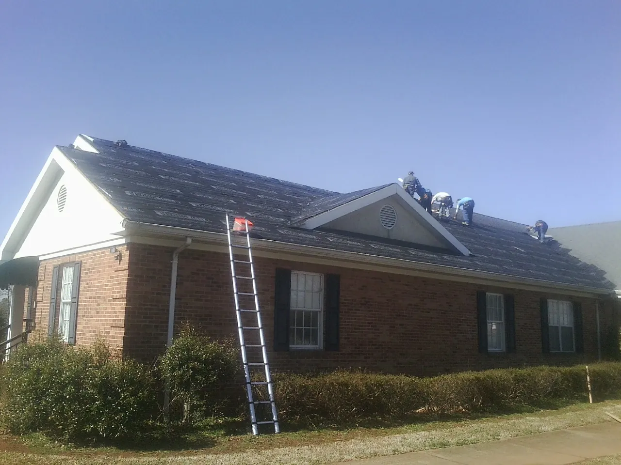 Crew tearing shingles off a brick ranch roof with a ladder set — Metal Roof Repair work by our crew in Mears
