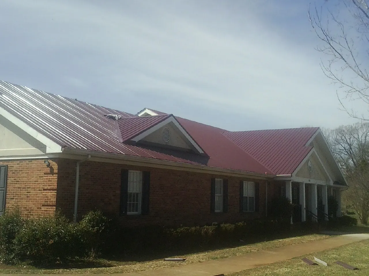Red metal roof with gabled entries on a long brick building, from a Hail Damage Roof Repair job in Mears