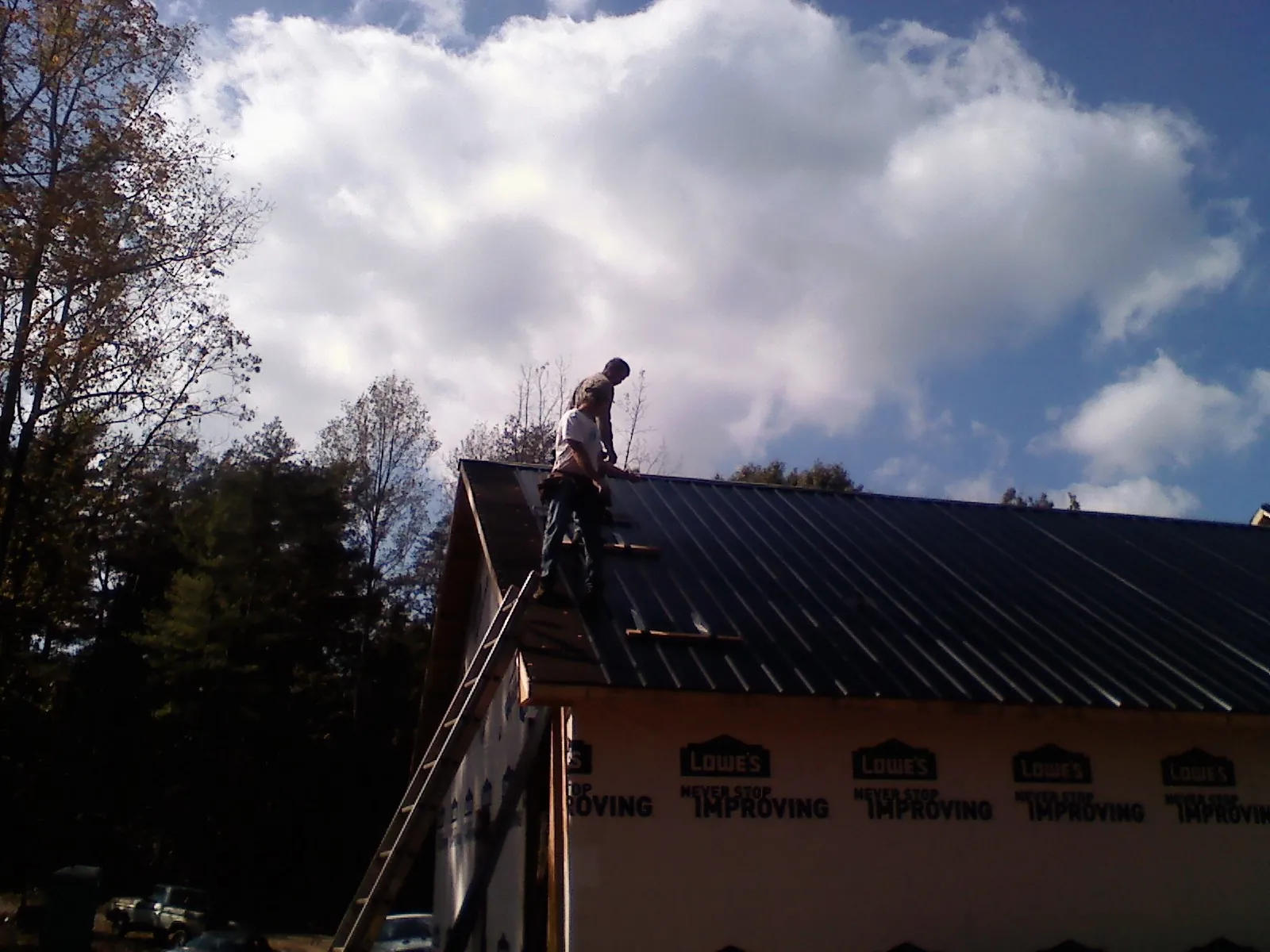 Roofer fastening dark metal panels high against a cloudy sky, from a Roof Inspection job in Mears