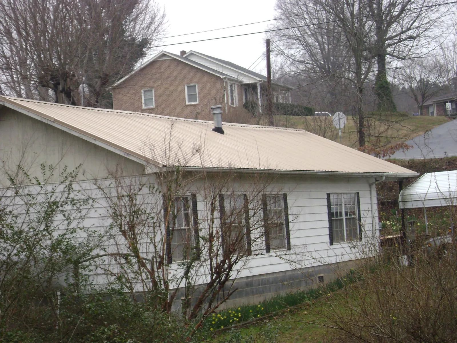 Tan metal roof on a white sided house set into a hillside — Commercial Roofing by Roofing Brothers in Mears