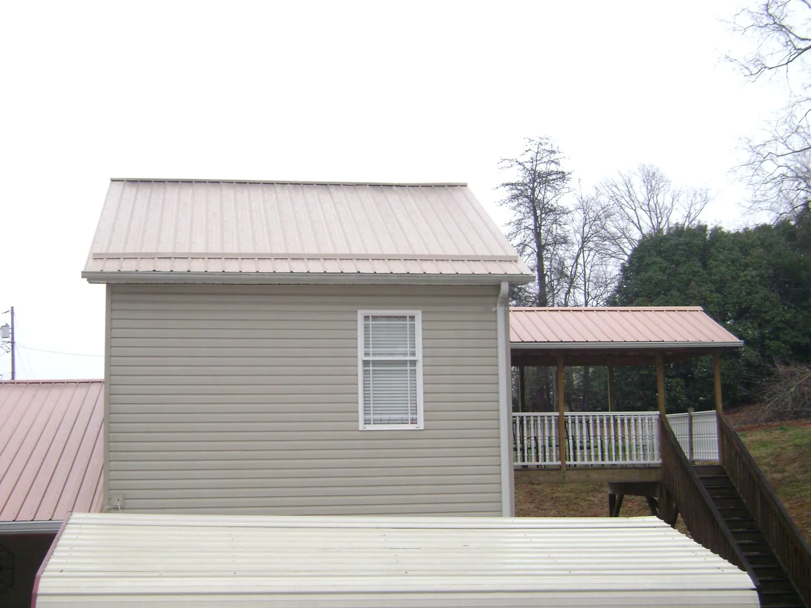 Tan metal roofs on a two story addition and attached porch, from a Roof Replacement job in Mears